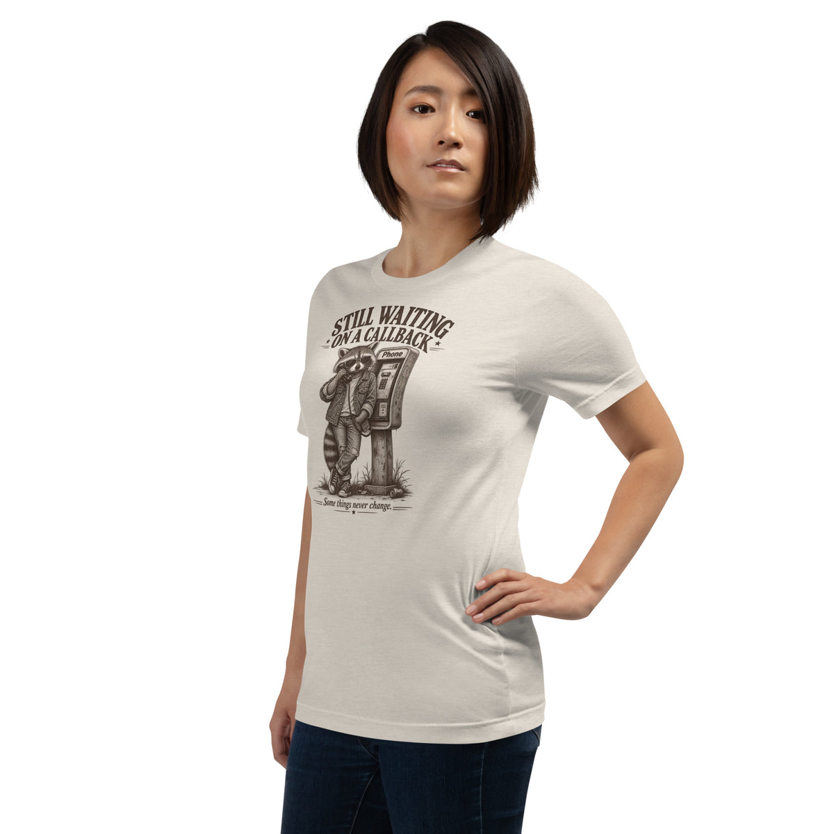 Female model wearing Still Waiting on a Callback funny raccoon graphic t-shirt in heather dust at a three-quarter side angle