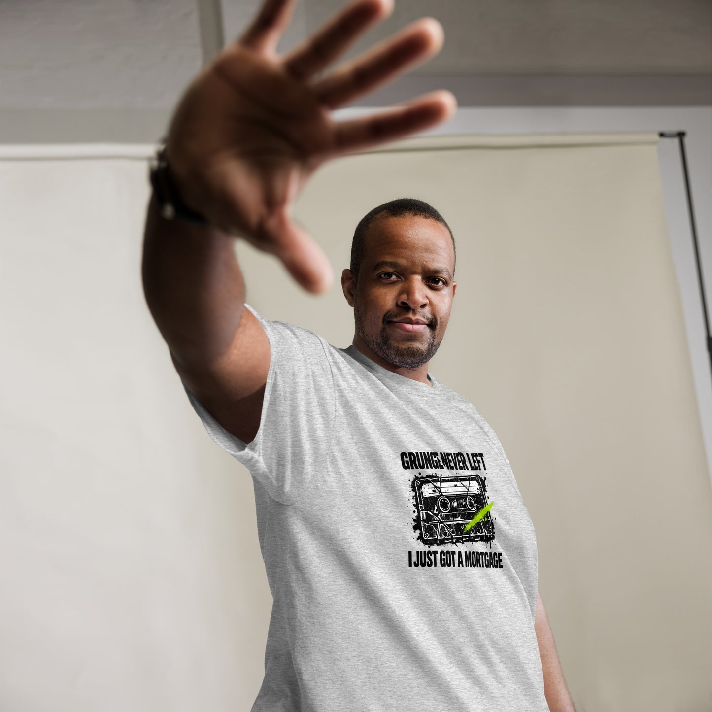 Male model reaching hand toward camera wearing an ash gray t-shirt with a vintage 90s cassette tape graphic reading "Grunge Never Left I Just Got a Mortgage"