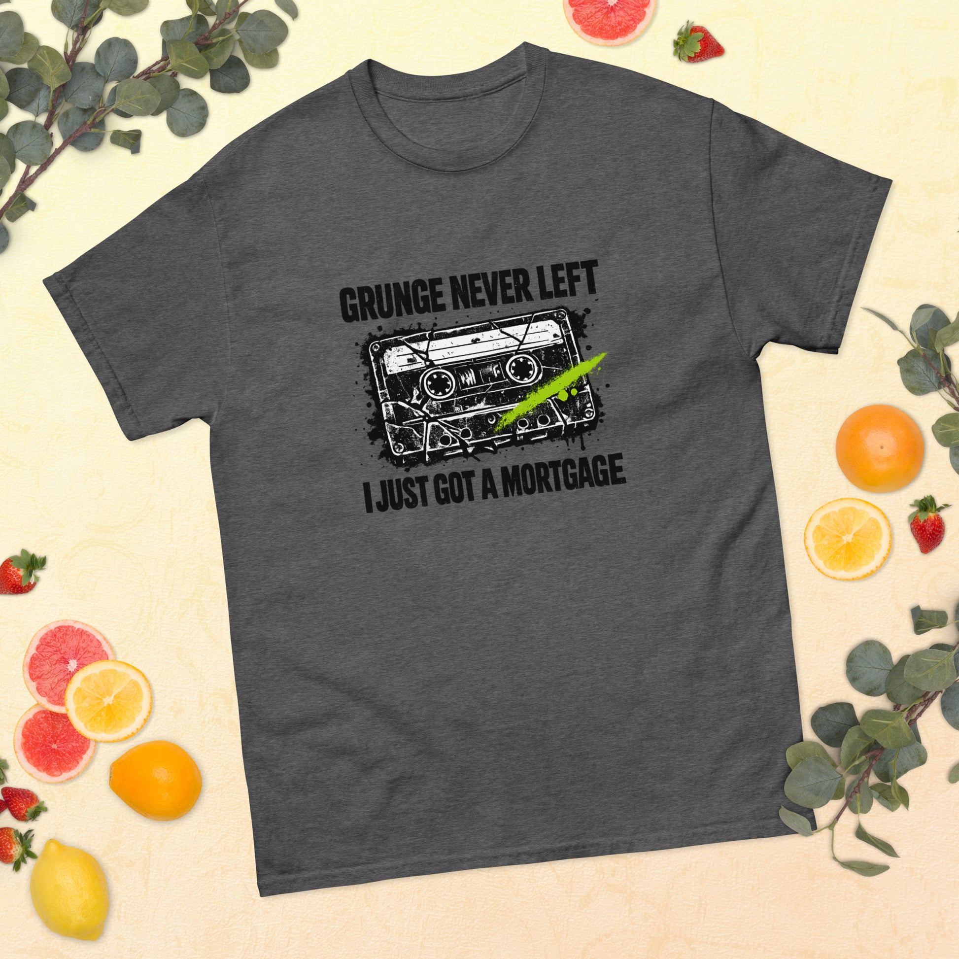 Flat lay mockup of a dark heather gray unisex t-shirt surrounded by sliced citrus fruit, strawberries, and greenery, featuring a 90s cassette graphic with the text "Grunge Never Left I Just Got a Mortgage"