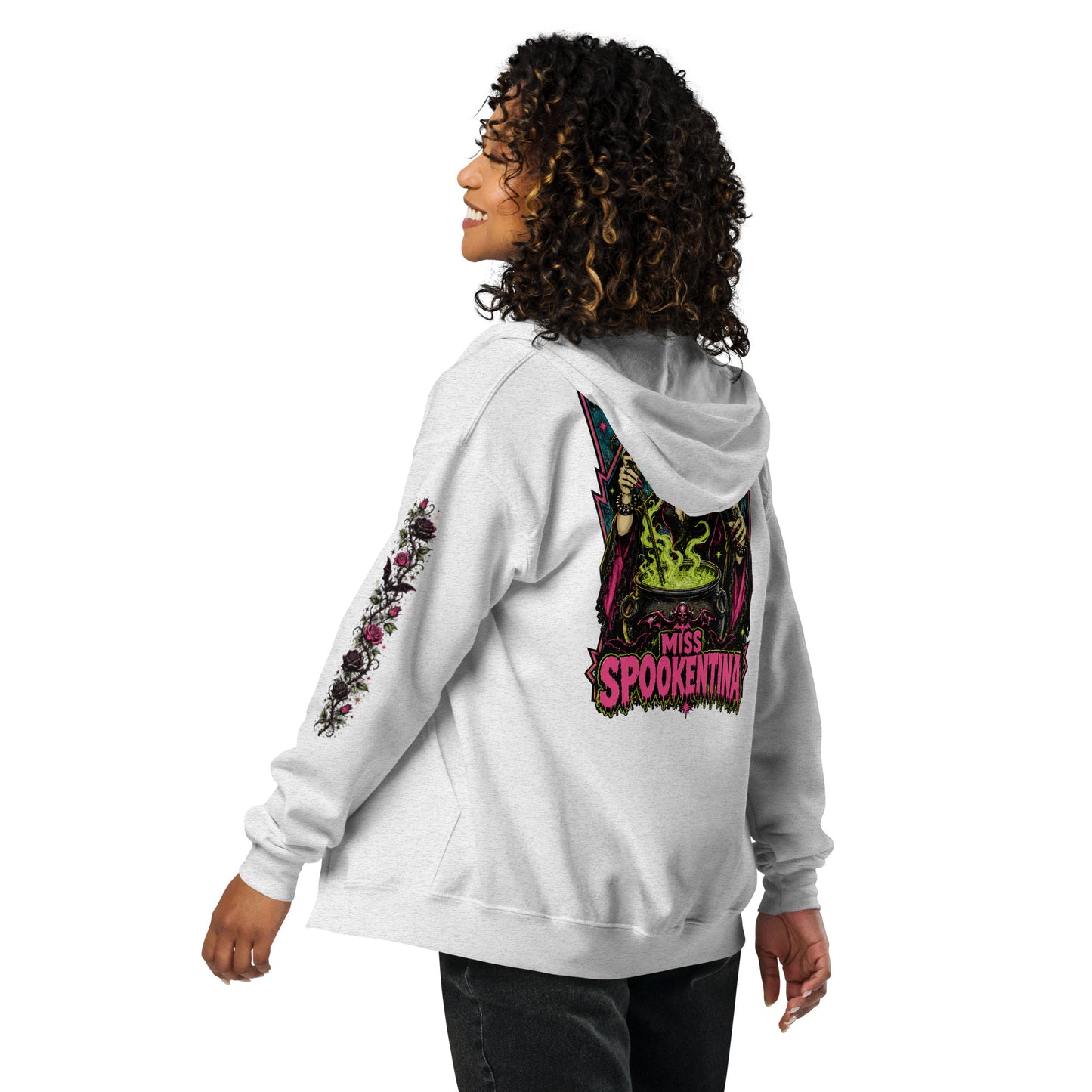 Back view of a female model wearing an ash grey unisex heavy blend zip hoodie featuring a vintage gothic witch brewing a cauldron with banner reading Miss Spookentina and floral sleeve print