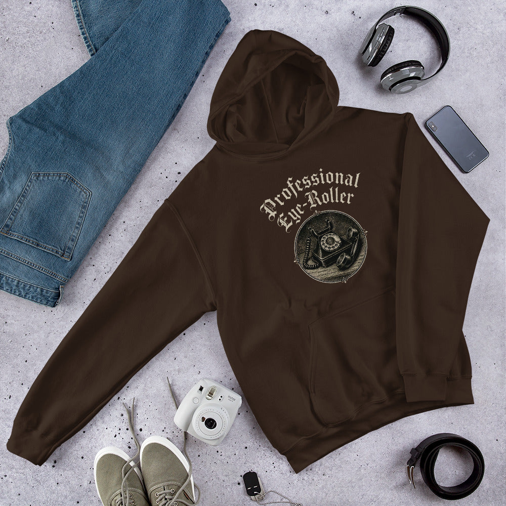 Folded flat lay styling of a dark chocolate brown hoodie featuring a retro Professional Eye-Roller graphic with headphones and beanie