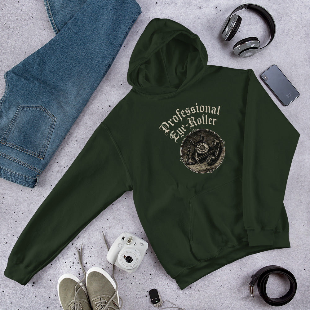 Folded flat lay styling of a forest green hoodie featuring a retro Professional Eye-Roller chest graphic with sunglasses and sneakers