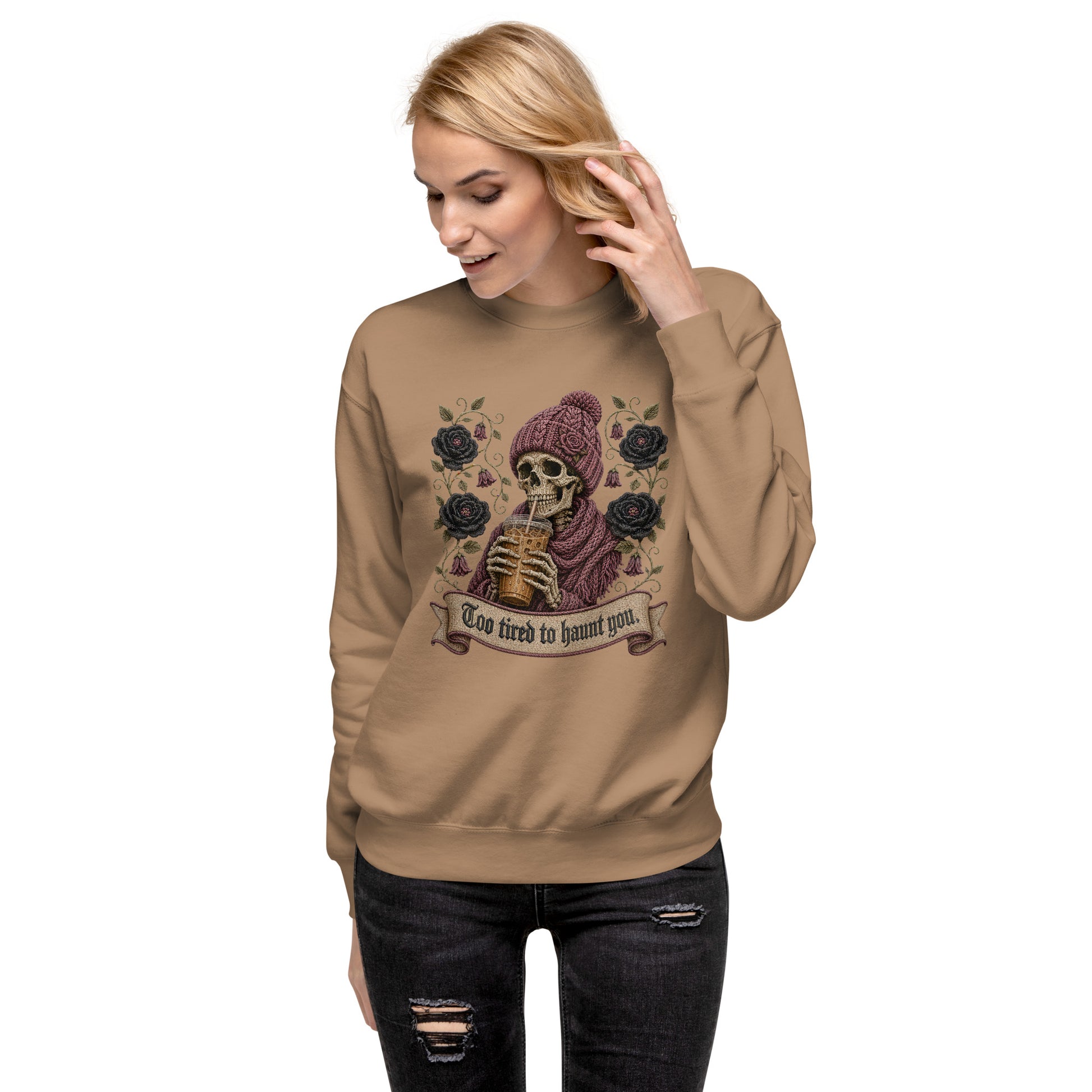 Female model wearing a carbon grey unisex crewneck sweatshirt featuring a gothic skeleton in a beanie drinking iced coffee with dark roses and banner reading "Too tired to haunt you"