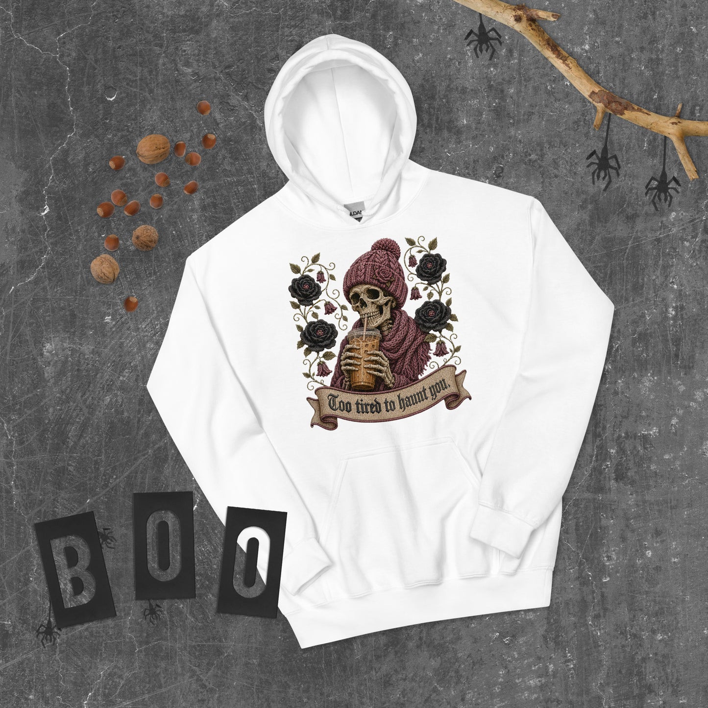 White unisex pullover hoodie flat lay mockup on dark rustic wood with spooky Halloween decor and BOO blocks featuring a gothic skeleton drinking iced coffee with Too Tired to Haunt You banner