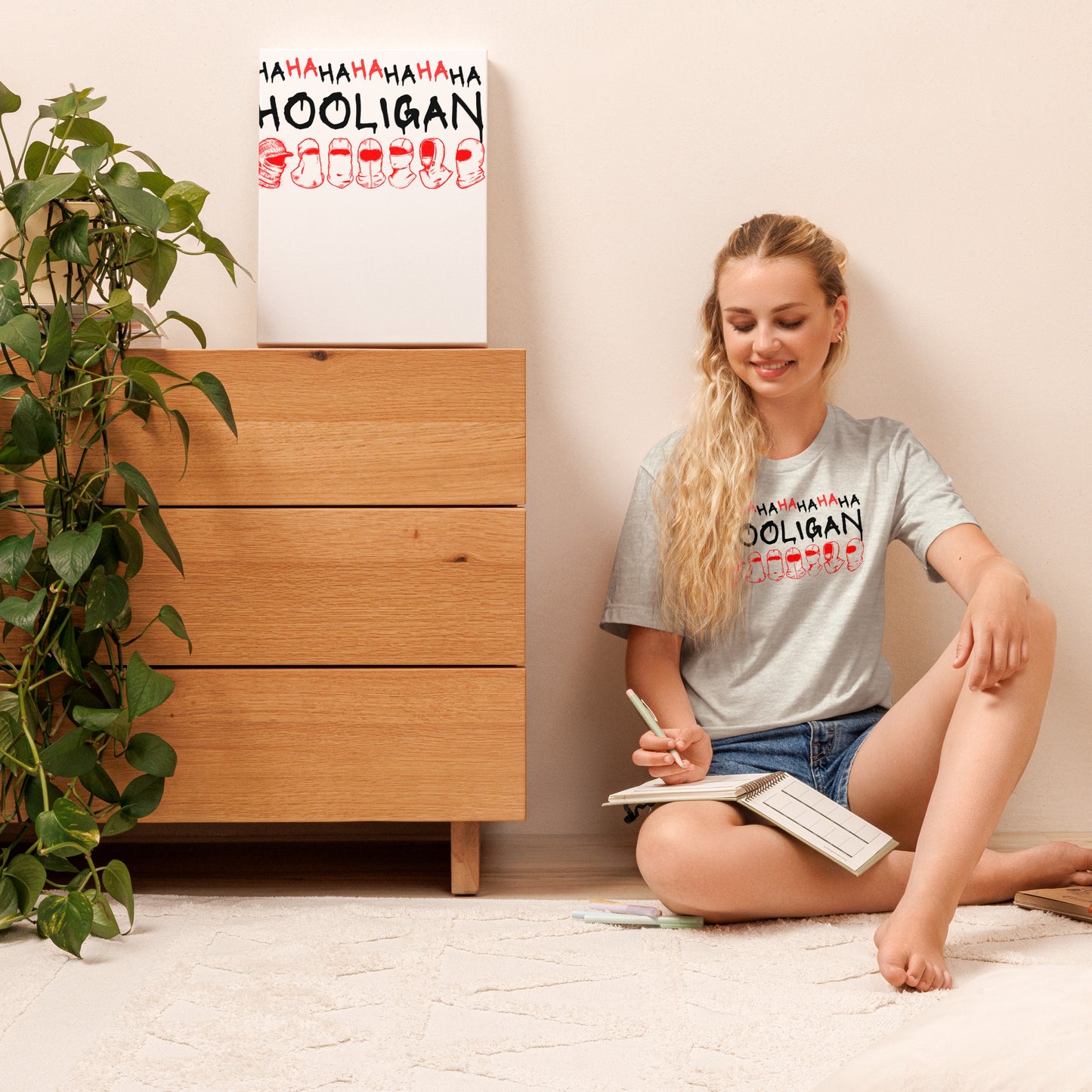 Model wearing the Ash gray BTS World Tour Hooligan unisex t-shirt while sitting on the floor in a casual home setting.