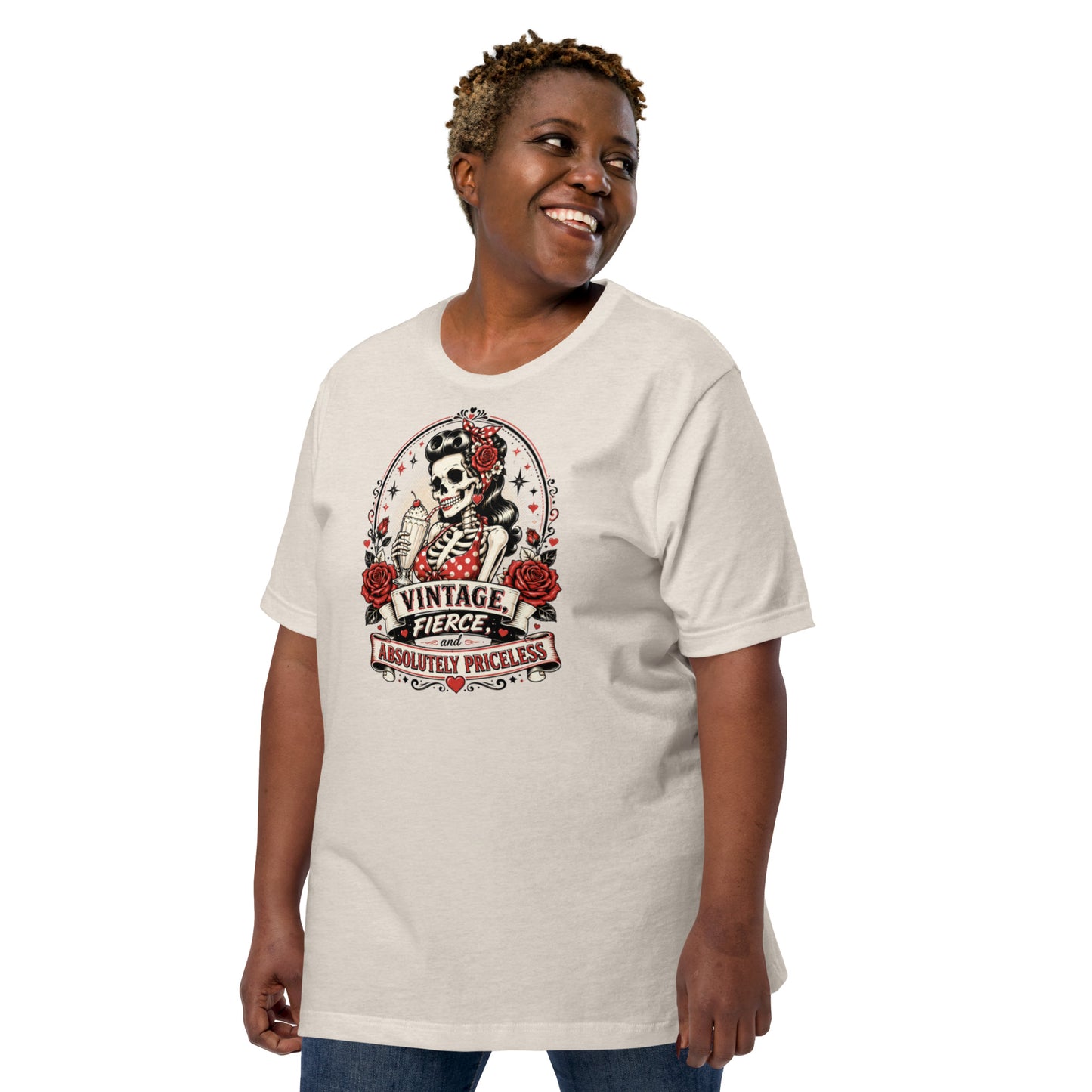 Front view of a smiling female model wearing a heather dust tan unisex graphic t-shirt featuring a rockabilly skeleton pinup girl holding a sundae with red roses and banner reading Vintage Fierce and Absolutely Priceless