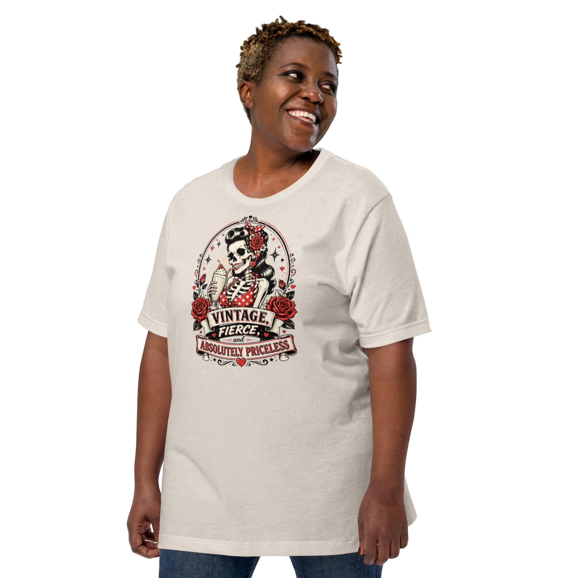 Front view of a smiling female model wearing a heather dust tan unisex graphic t-shirt featuring a rockabilly skeleton pinup girl holding a sundae with red roses and banner reading Vintage Fierce and Absolutely Priceless